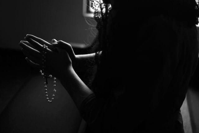 Black and White image of woman, neck down, with hands holding Rosary